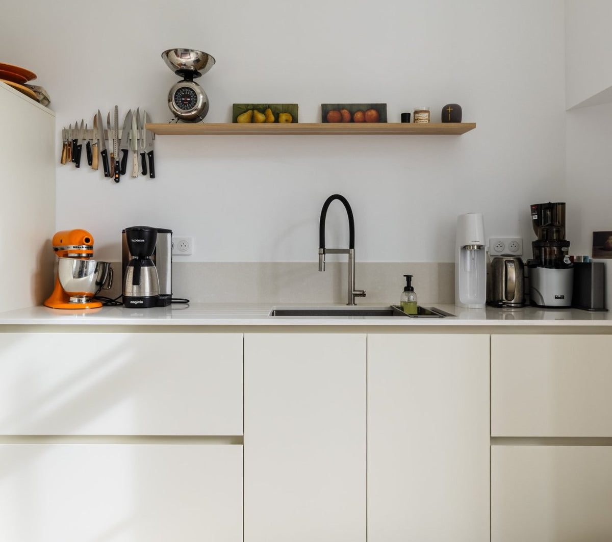 Arrière-cuisine aux façades blanc cassé avec évier sous plan, mitigeur à douchette et étagère en chêne