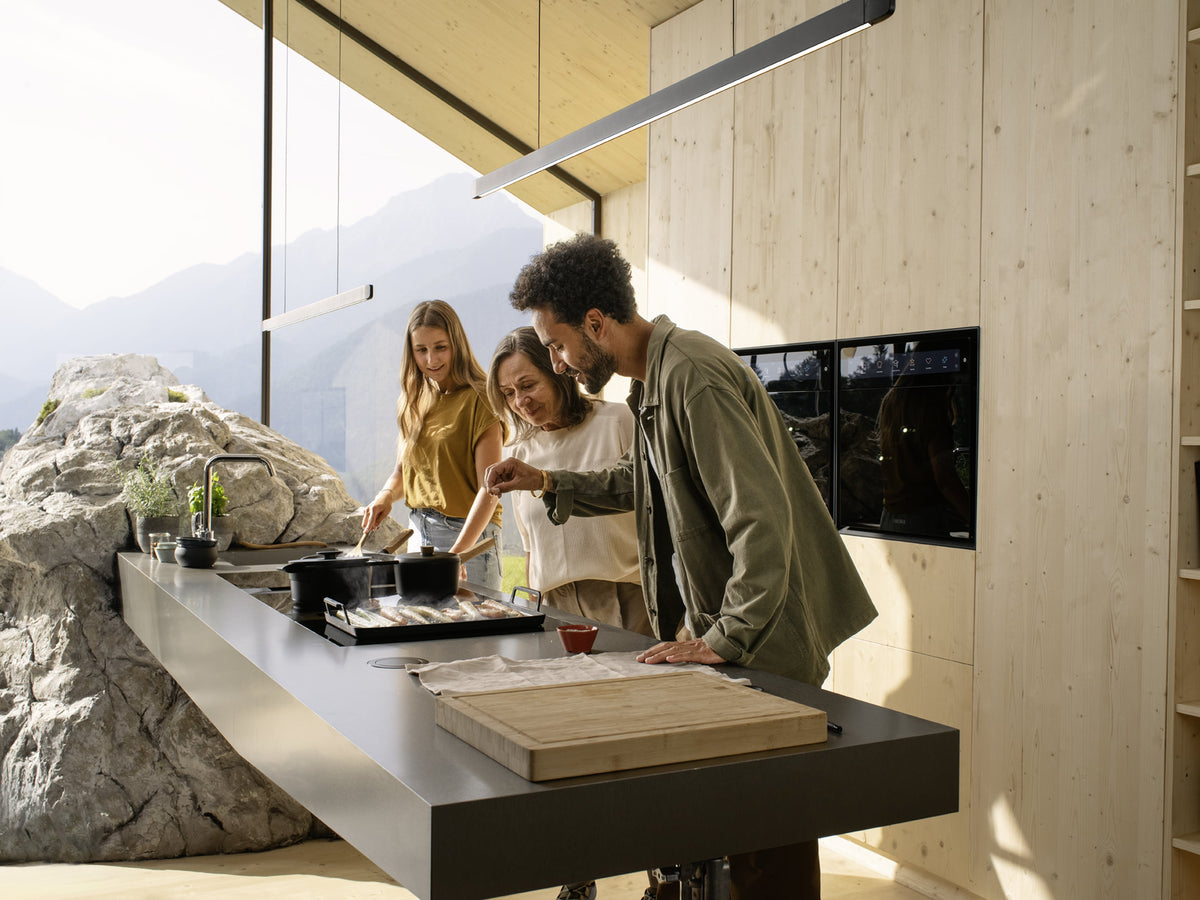 Suspension BORA Horizon noire au-dessus d’un îlot de cuisine où cuisinent trois amis