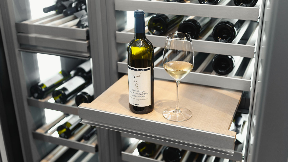 Bouteille de vin blanc et verre posés sur une tablette sortie d’une cave à vin Liebherr Monolith