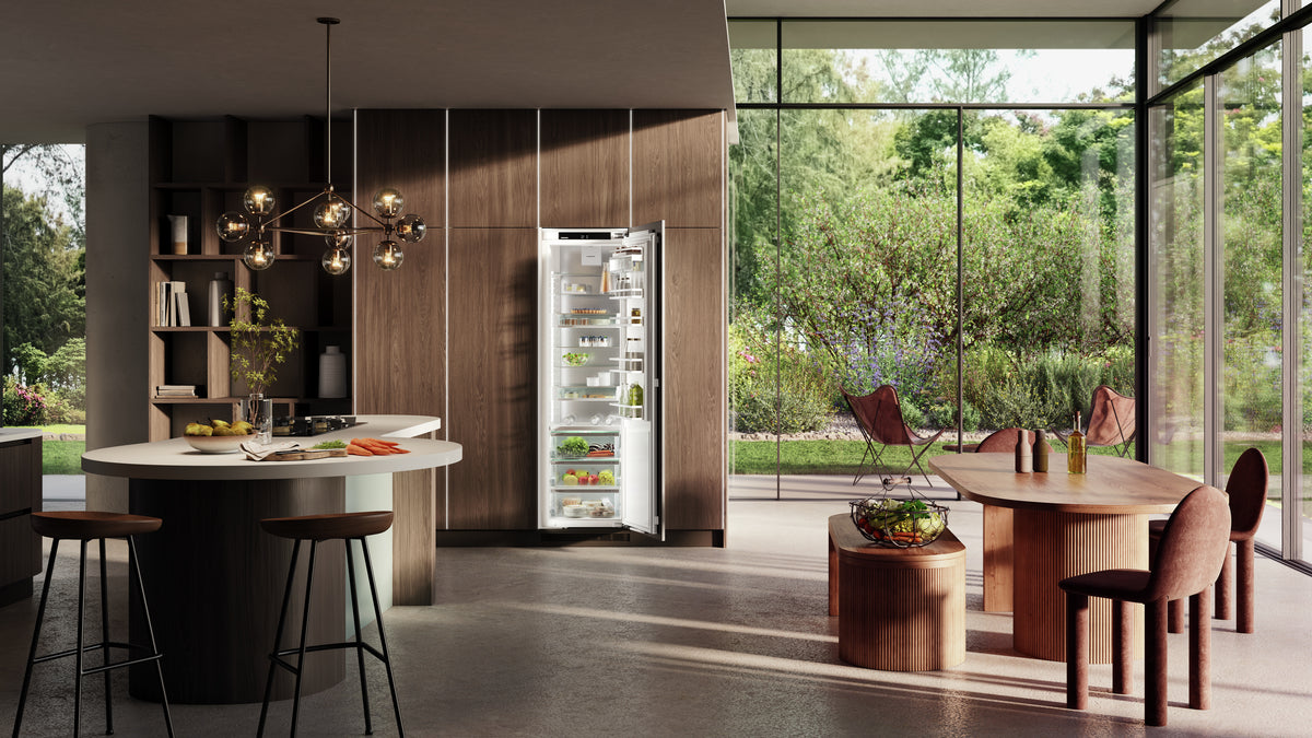 Réfrigérateur encastrable Liebherr ouvert dans une cuisine en bois sombre ouverte sur le jardin