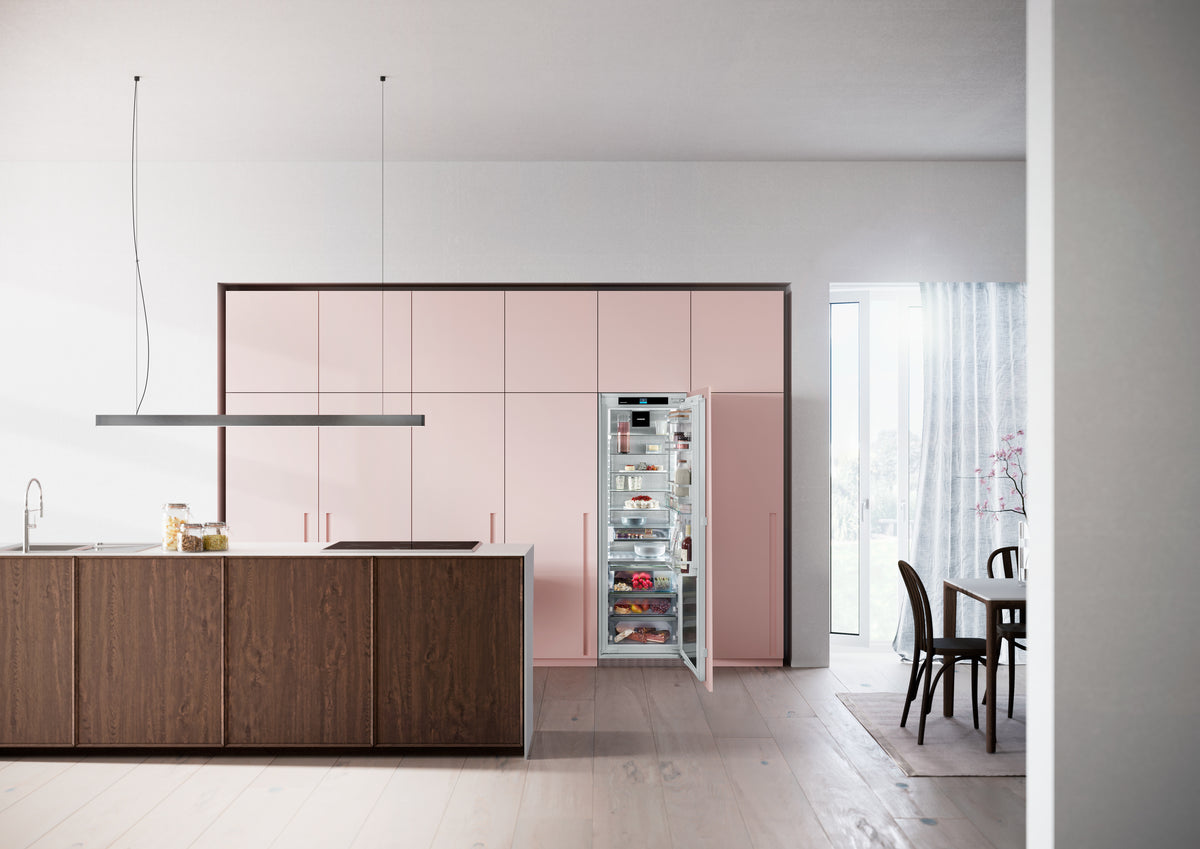 Réfrigérateur encastrable Liebherr ouvert dans une cuisine aux façades rose poudré et à l’îlot en bois