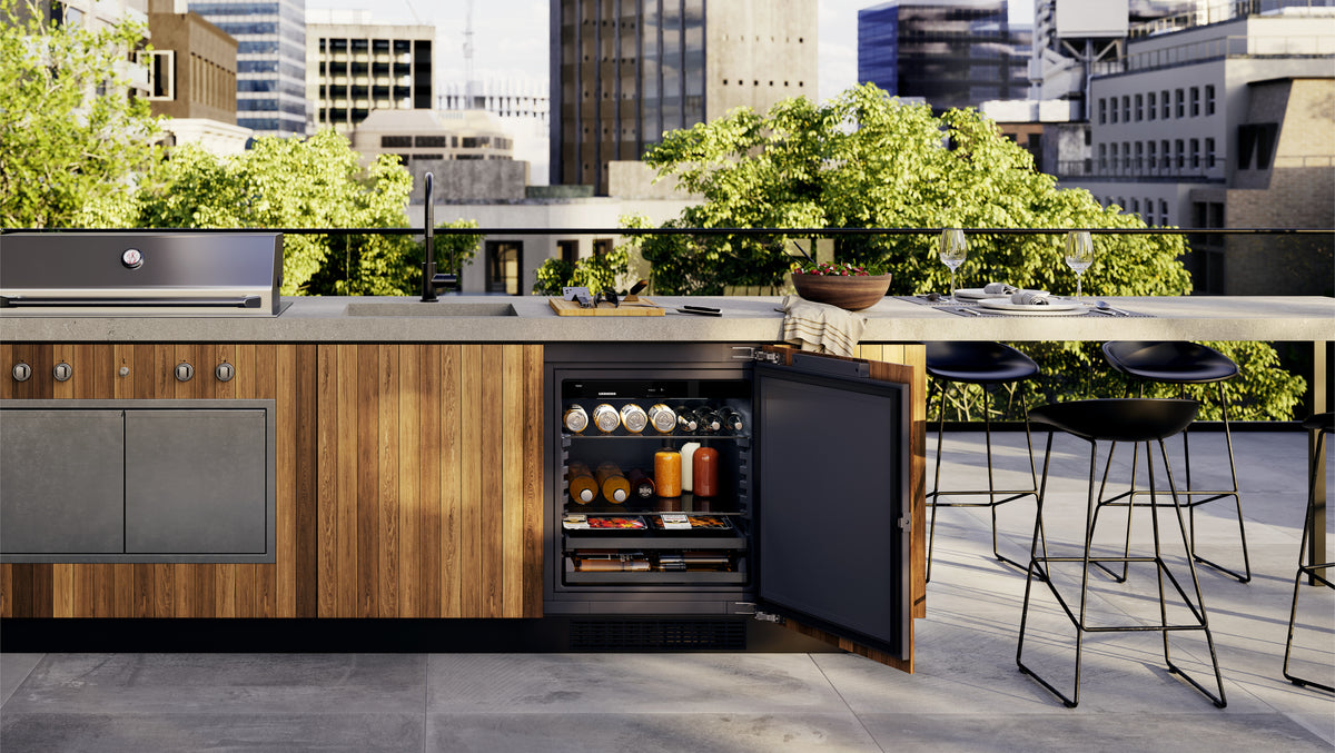 Réfrigérateur d’extérieur Liebherr ouvert sous le plan d’une cuisine d’été en bois, sur une terrasse