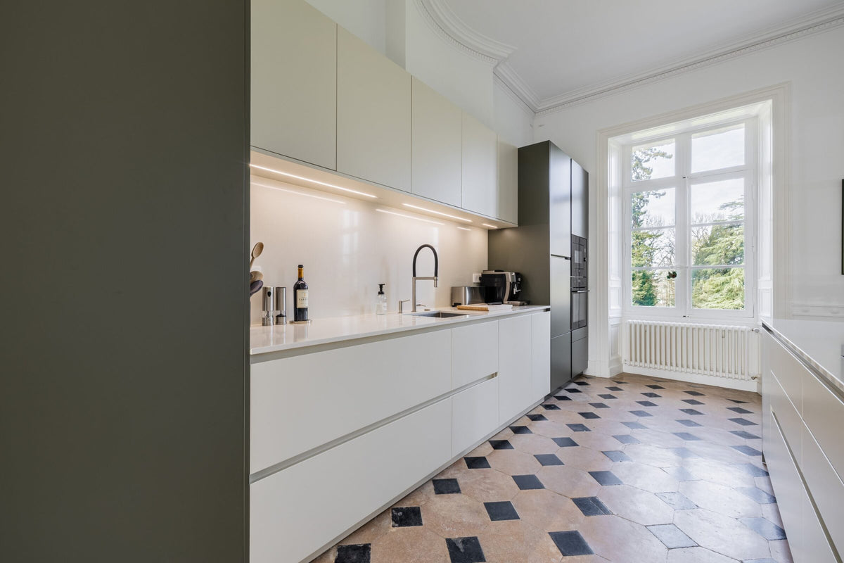 Linéaire de cuisine blanc cassé avec crédence en Silestone face à une grande fenêtre